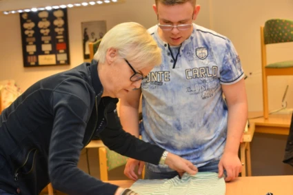 Lärare tillsammans med en elev viker en tröja.