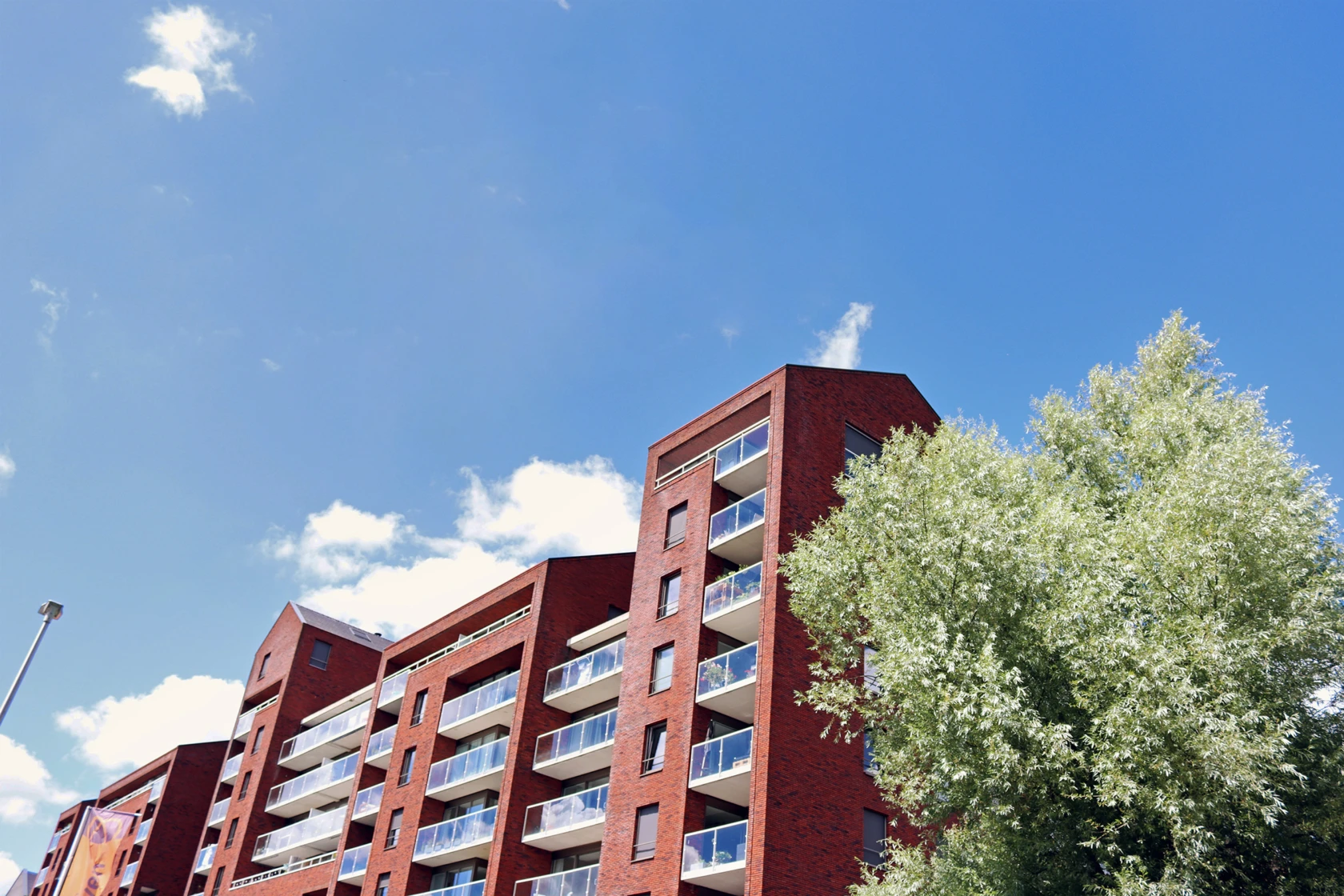 ETt lägenhetshus vid ett grönt träd och med en blå himmel i bakgrunden.