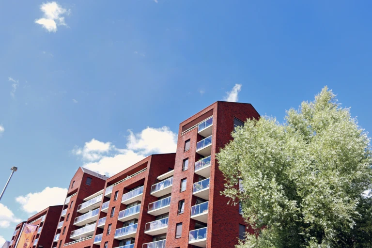 ETt lägenhetshus vid ett grönt träd och med en blå himmel i bakgrunden.