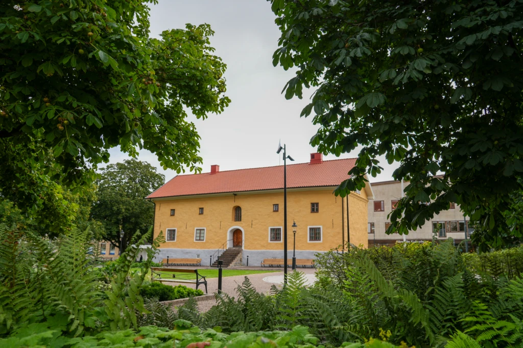 Gul museibyggnad omringad av gröna träd och växter.