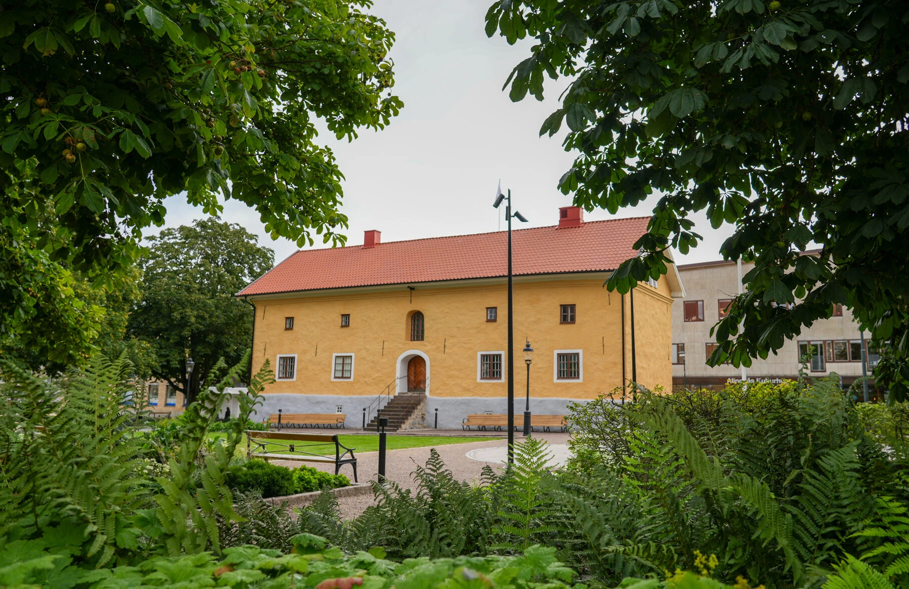 Gul museibyggnad omringad av gröna träd och växter.