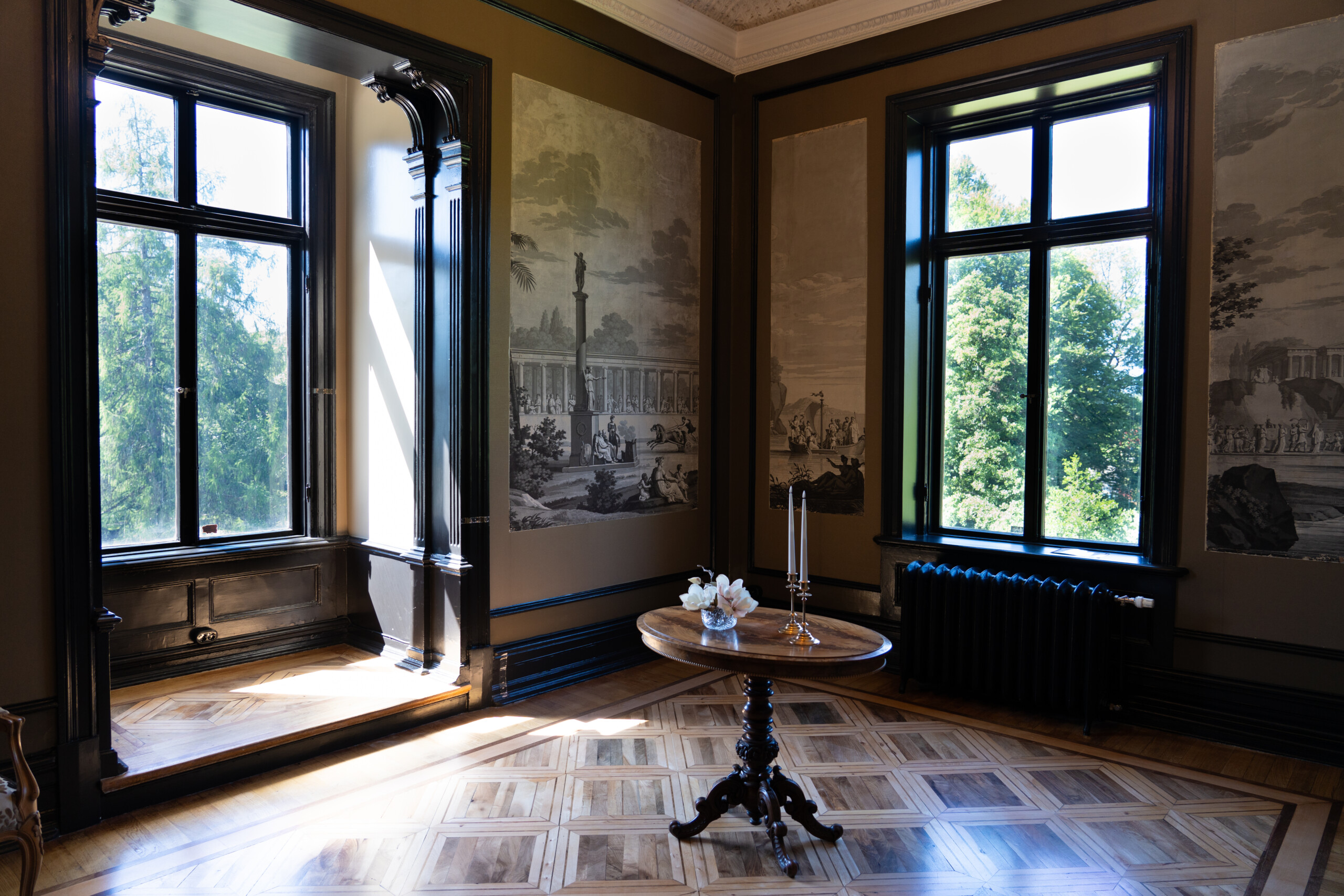 Fint inrett rum i bruna färger med två stora fönster och ett bord i mitten.