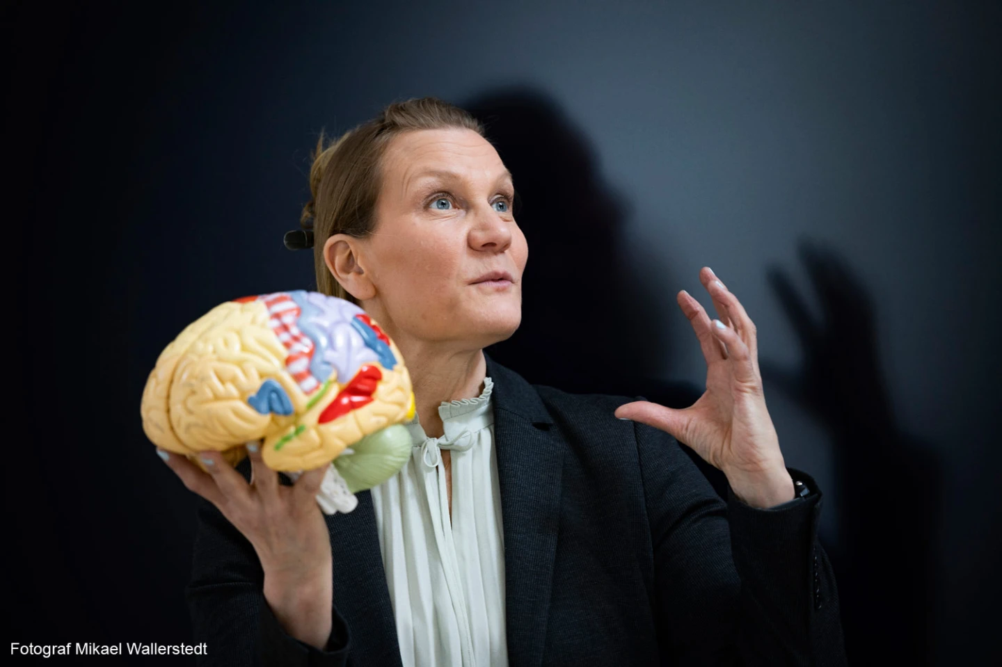 En kvinna som tittar snett uppåt och håller en hjärna i plast i sin ena hand.
