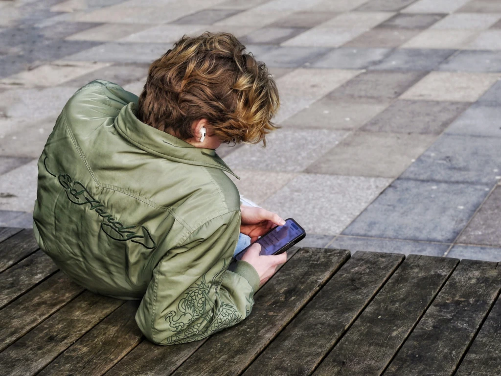 Kille ligger halvt ner på sidan och kollar i telefonen.