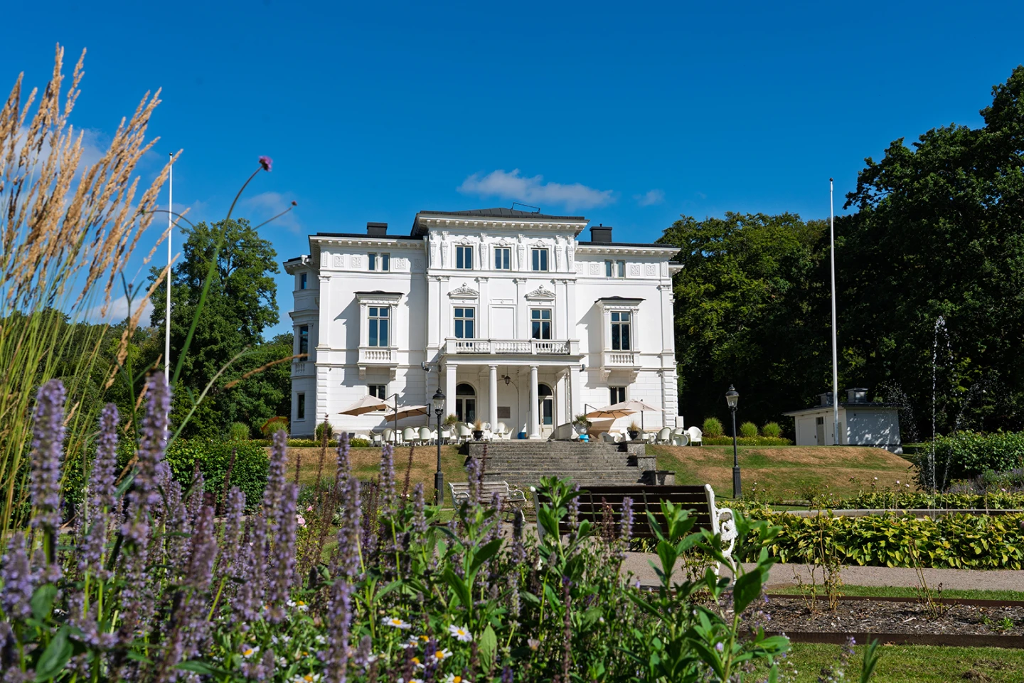 Vit slottsliknande byggnad i gröna omgivningar.