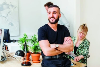 Kille med mörkt skägg står med korslagda armar och ser glad ut.