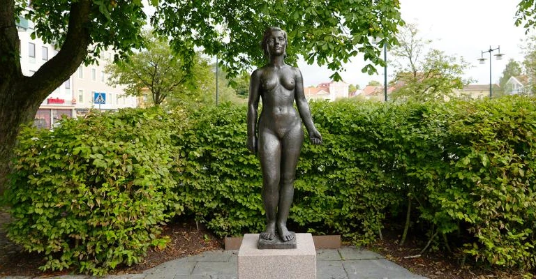 En staty av en kvinna i en park på sommaren.