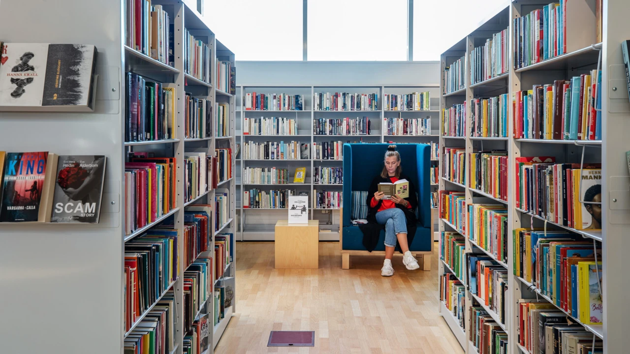 En kvinna sitter och läser på bibliotekets vuxenavdelning.