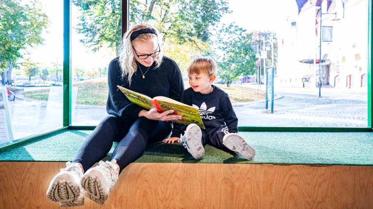 Mamma och barn läser bok på biblioteket.