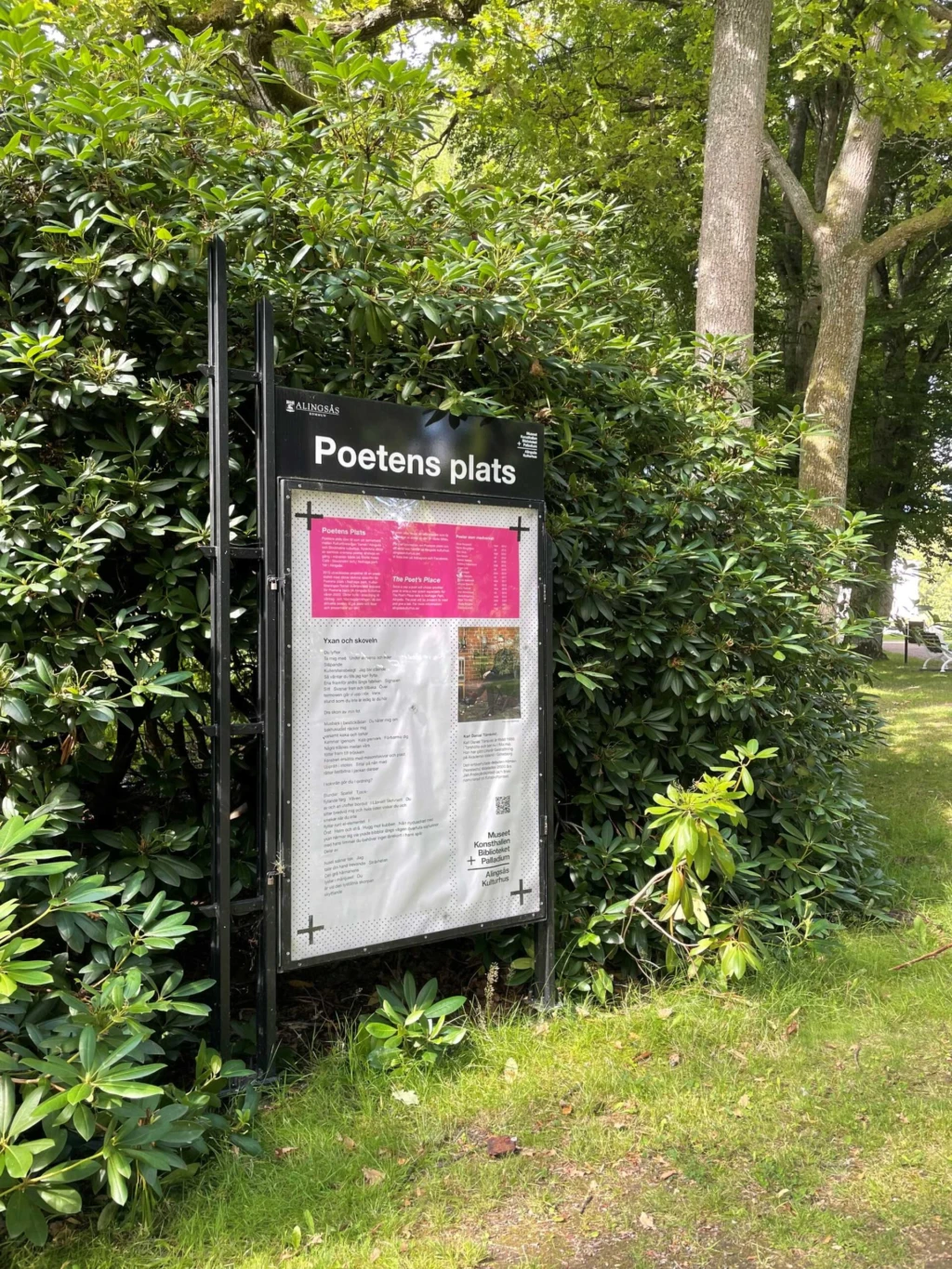 En skylt med text. Grönskande buskage i bakgrunden.