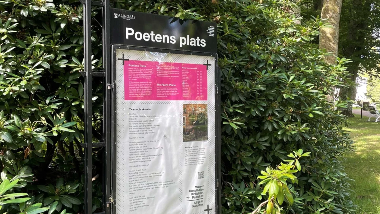 En skylt med text. Grönskande buskage i bakgrunden.