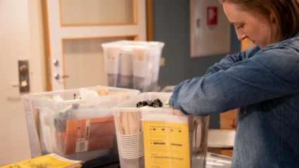En kvinna packar transparanta plastlådor med beredskapsmateriel. I lådan finns bland annat engångsbestick, broschyren "Om krisen eller kriget kommer" samt våtservetter.
