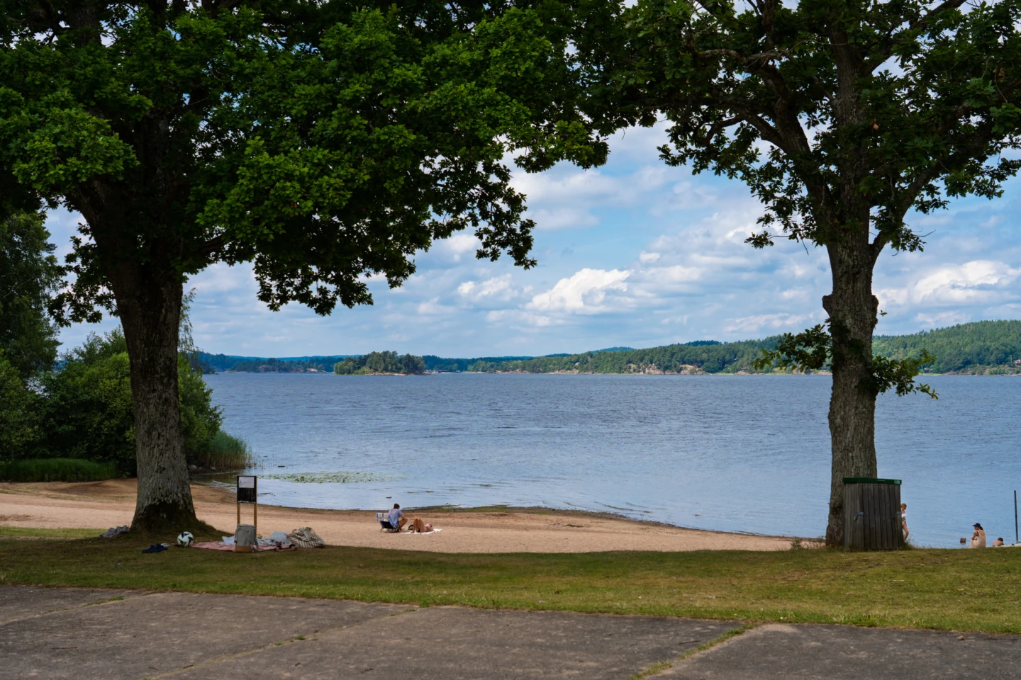Playa Mjörn med moln på himlen och träd i förgrunden.