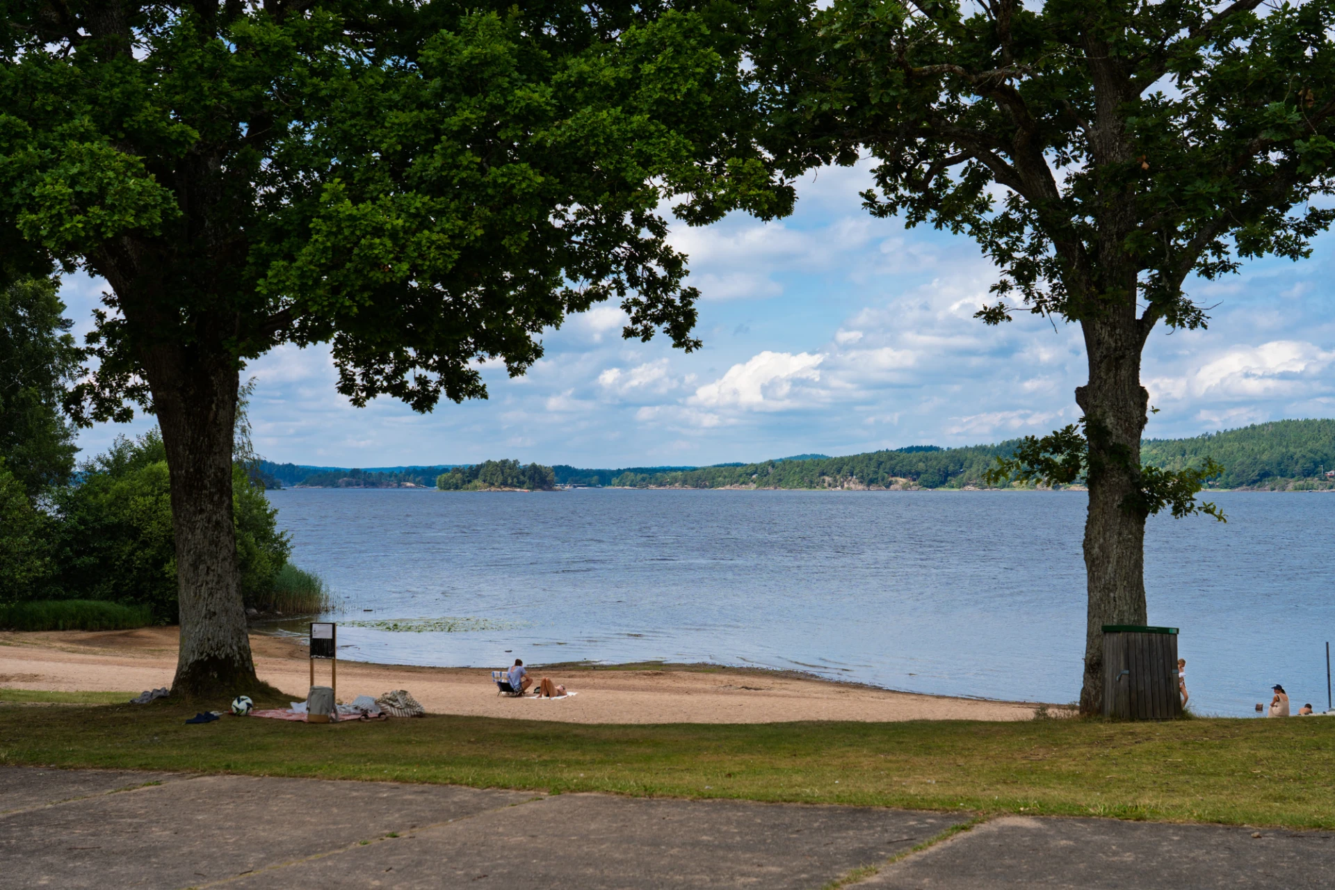 Playa Mjörn med moln på himlen och träd i förgrunden.