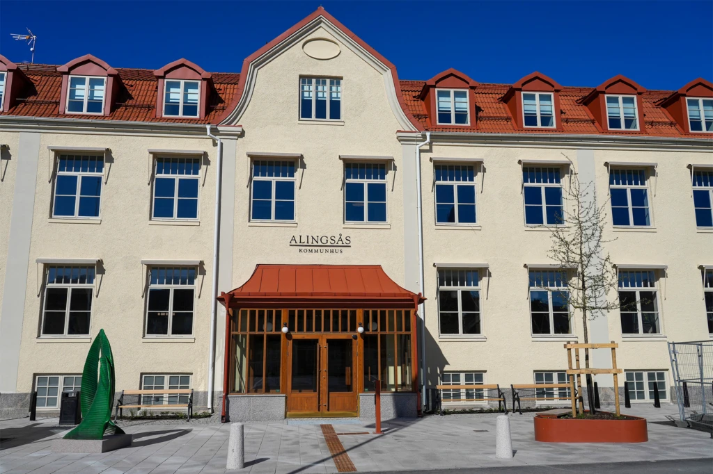 Framsidan av Alingsås nya kommunhus. Ett ljusgult hus med rött tak och flera fönsterrutor.