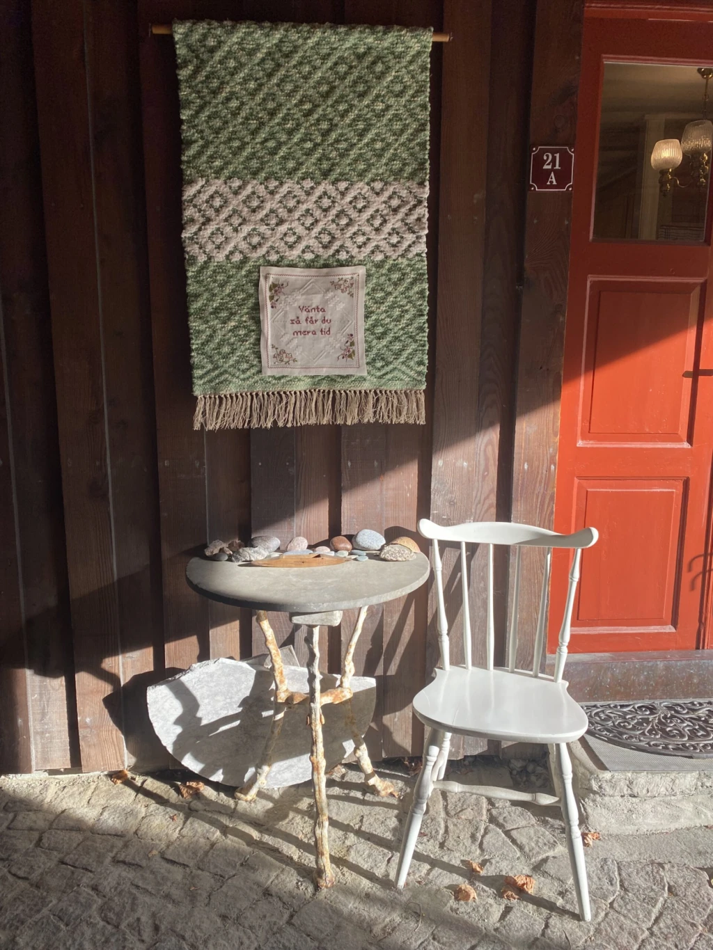 stol står vid röd dörr, det hänger vävduk på väggen bakom