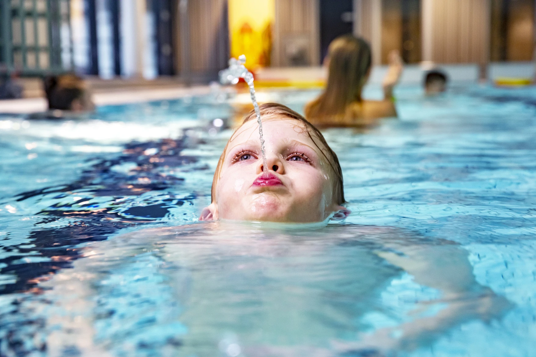 Pojke i bassäng som sprutar vatten.