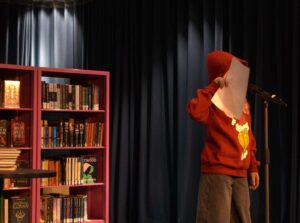 En ung person håller i ett papper och har på sig röd tröja