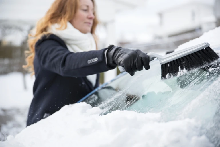 En kvinna som sopar av snön från sin bil.