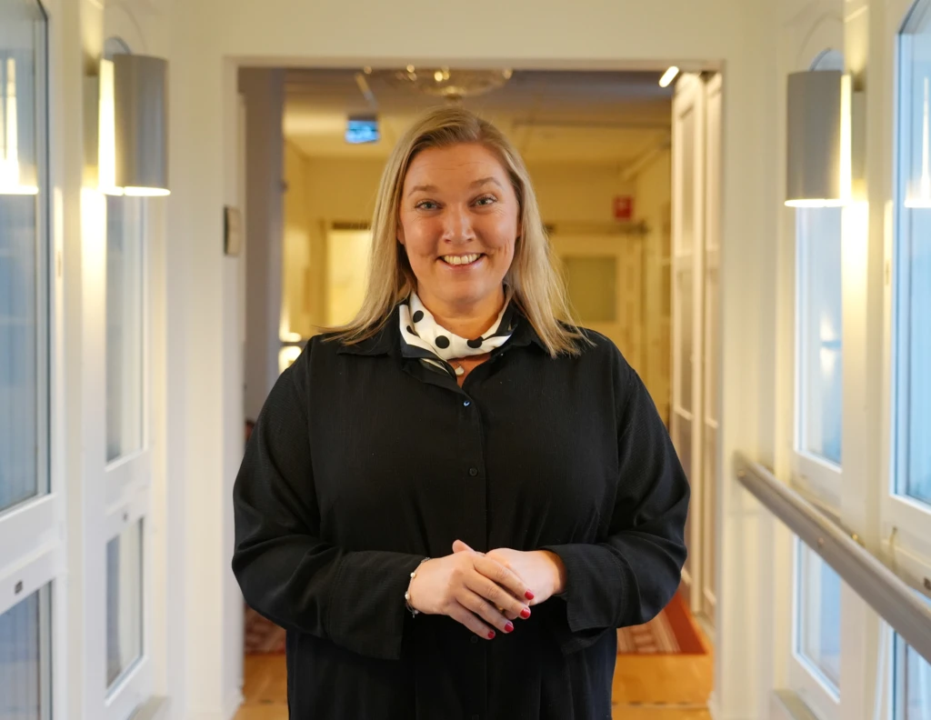 Medelålders kvinna i ljust mellanlångt hår kollar in i kameran och ser glad ut.