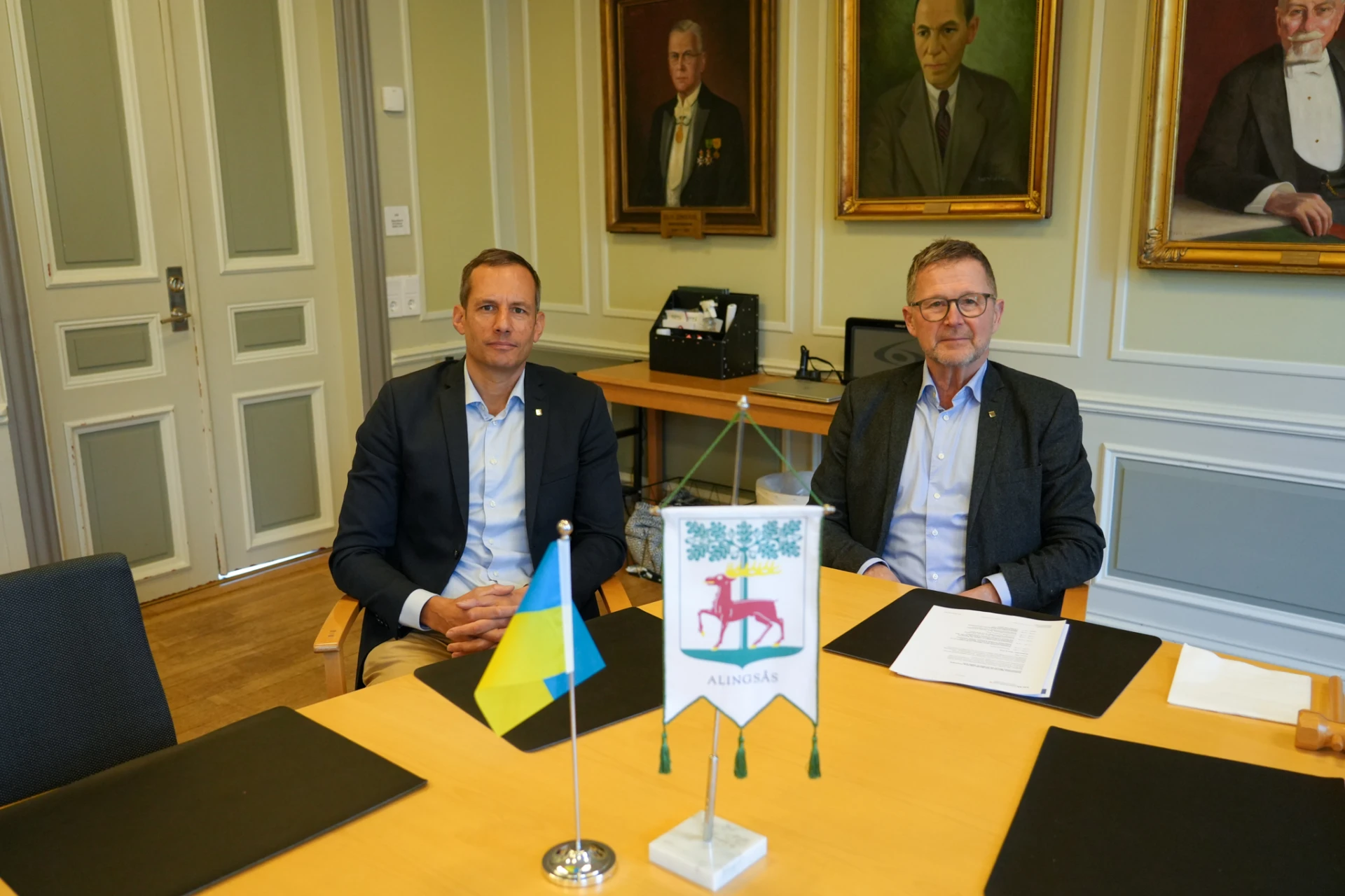 Kommunstyrelsens vice ordförande Anton César (S) och ordförande Jan-Erik Wallin (M) sitter vid ett bord med Ukrainas flagga.