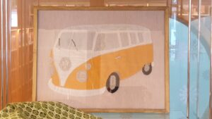 En tavla i ett glasskåp, föreställer en minibuss i gult och vitt