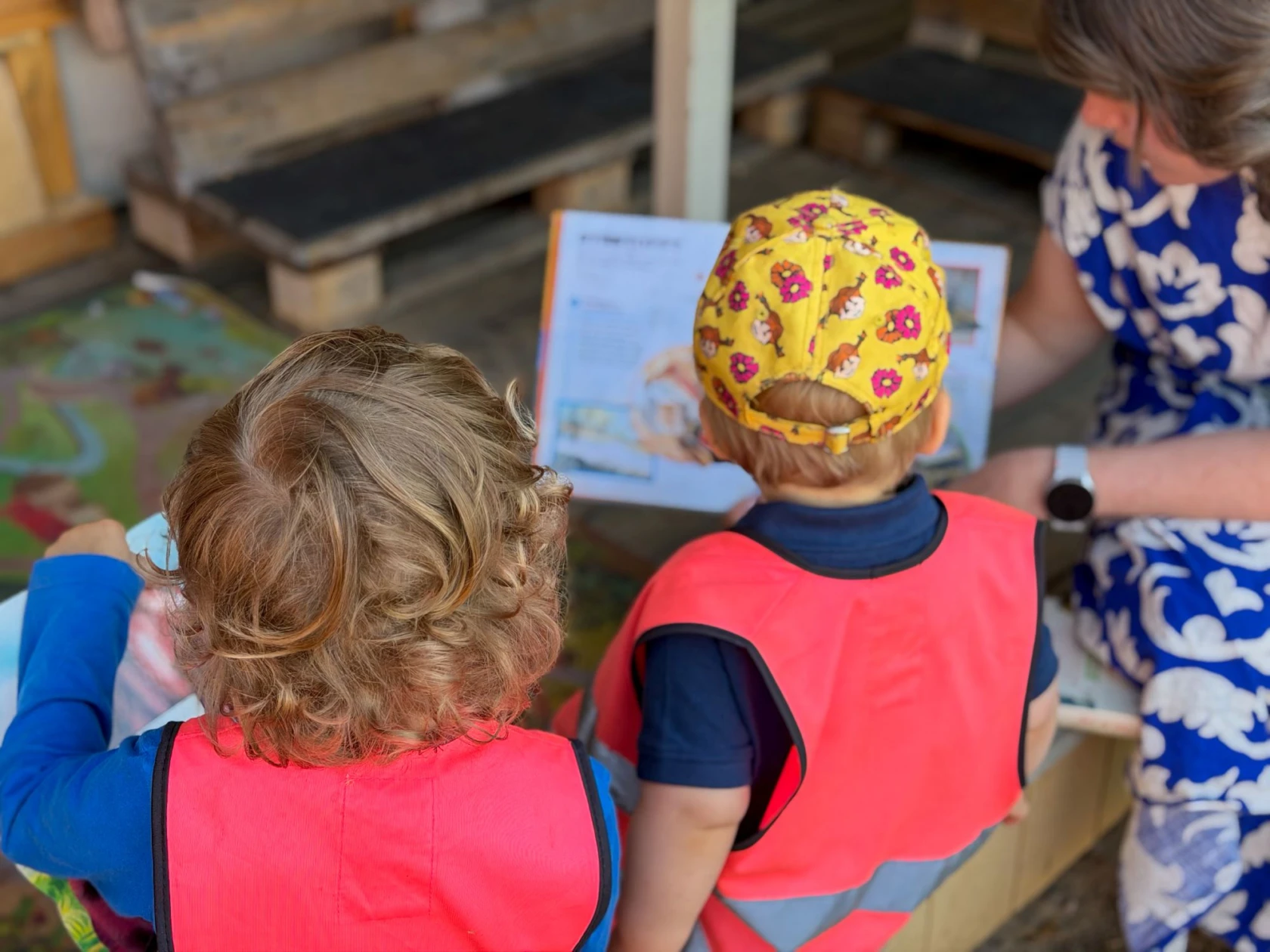 Två barn läser med pedagog utomhus