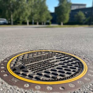 foto av ett brunnsluck med text på. träd i bakgrunden