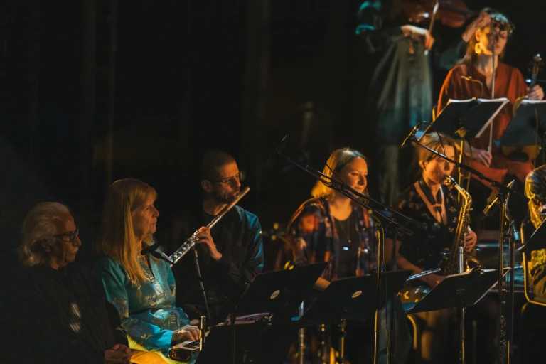 En orkester spelar, olika personer spelar olika instrument. Scenljus