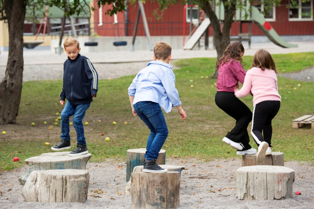 Fyra elever hoppar på stubbar på skolgård.