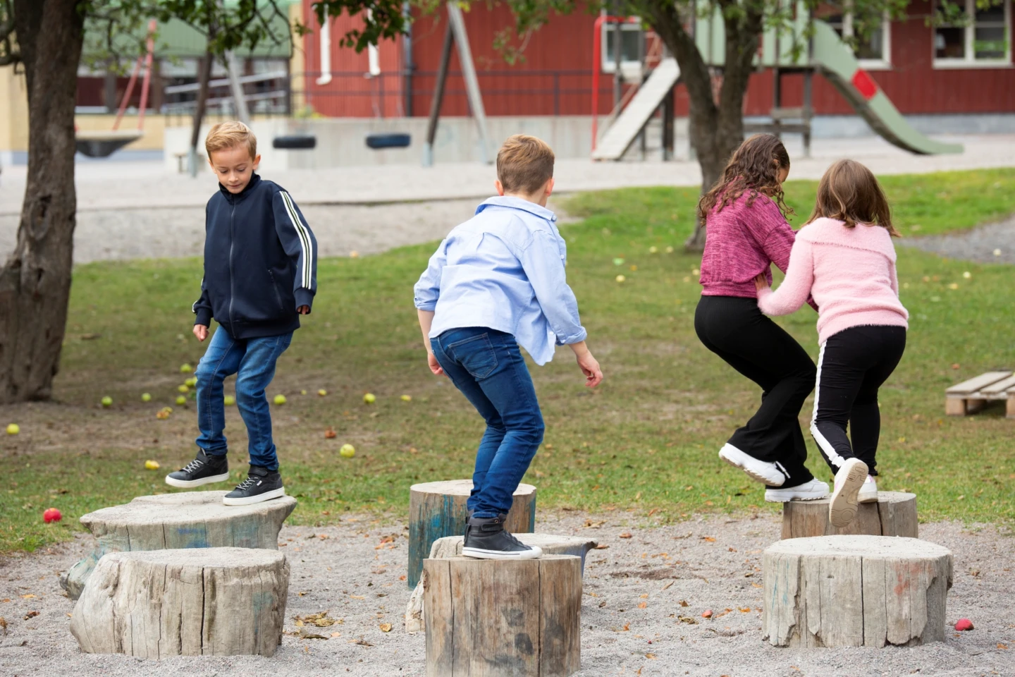 Fyra elever hoppar på stubbar på skolgård.